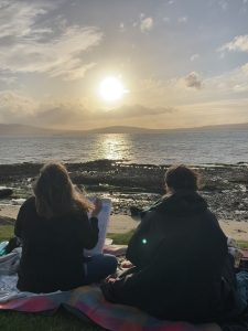 Two women painting on a beach at sunset — a simple self-care moment that reflects connection, calm, and creativity, supporting emotional wellbeing and mental health. Counselling in Belfast and online and in person support.