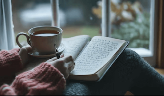 Person journalling with a warm cup of tea during quiet self-reflection